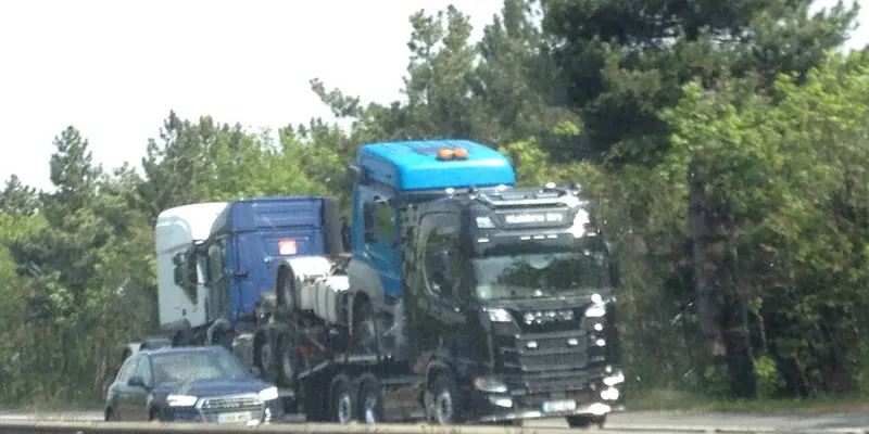 Un porte-camions transporte des tracteurs routiers neufs sur une route.
