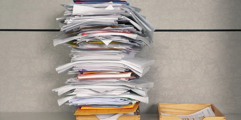 Une pile de dossiers et de documents à côté de corbeilles à courrier.