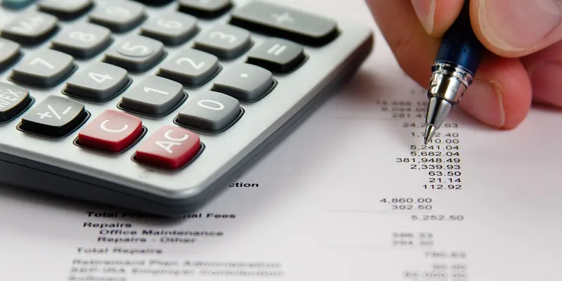 Une main annote un relevé de chiffres à côté d’une calculatrice.
