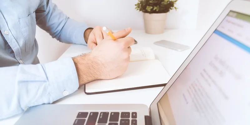 Un homme prend des notes dans un carnet, devant son ordinateur portable.