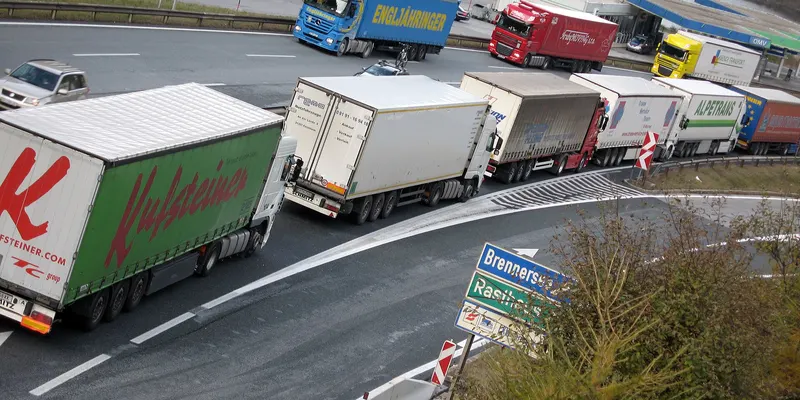 Une file de poids lourds de plusieurs entreprises sur une route de montagne.