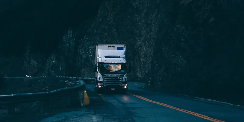 Un poids lourd roule de nuit sur une route de montagne bordée de glissières.
