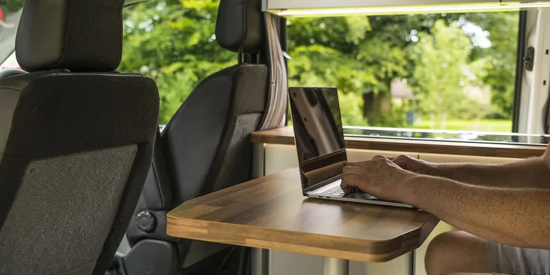 Une personne travaille sur un ordinateur portable installé dans un véhicule aménagé.
